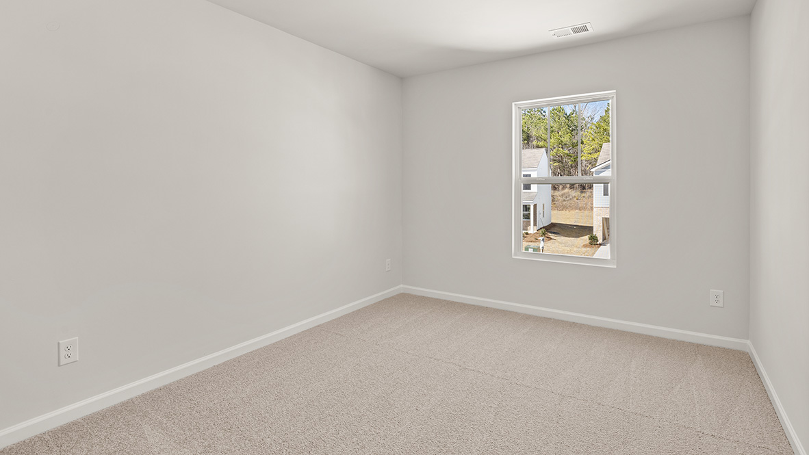 Empty room with soft beige carpet and light gray walls. A single window reveals a view of suburban houses and trees, creating a calm ambiance.