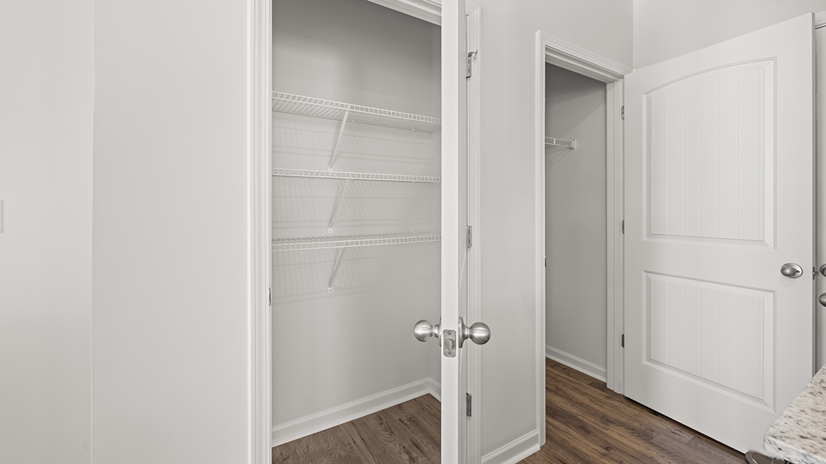 Two open white closet doors reveal empty, white wire-shelved storage spaces. The room has wooden floors and a modern, minimalist feel.
