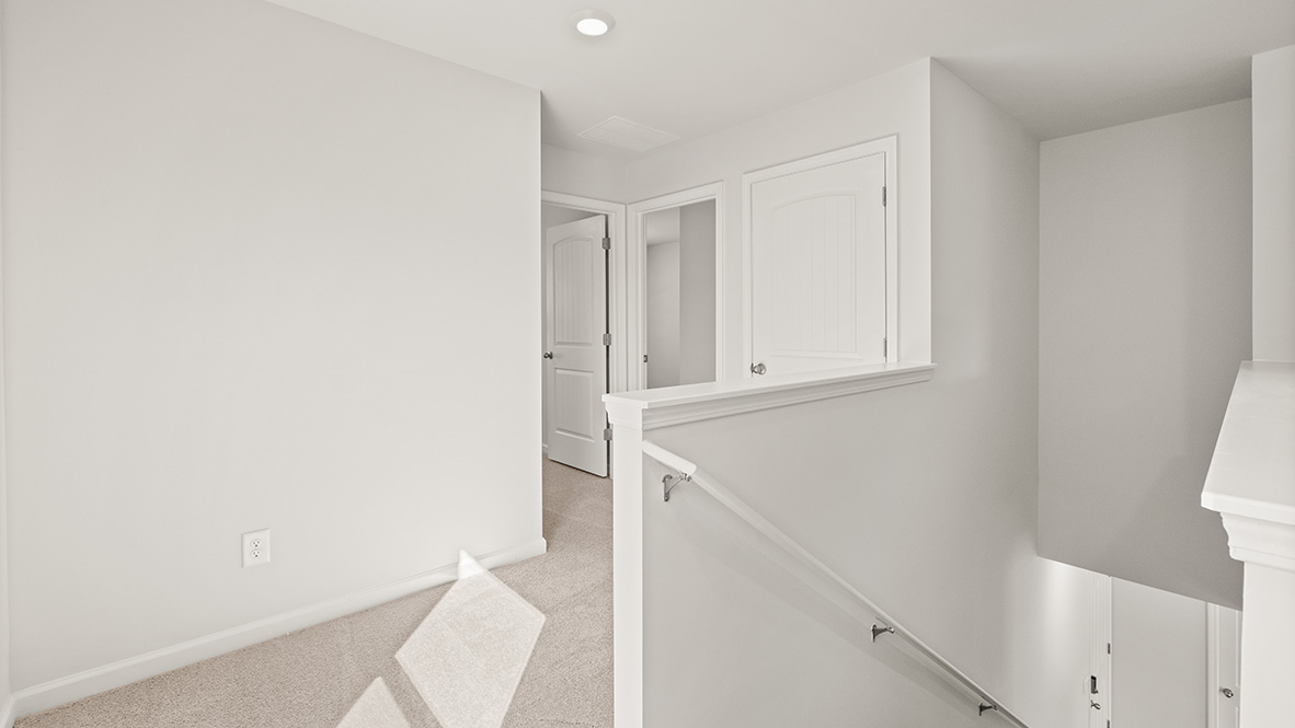 A bright hallway with soft beige carpet and white walls, featuring two white doors and a modern staircase railing. The space feels open and airy.