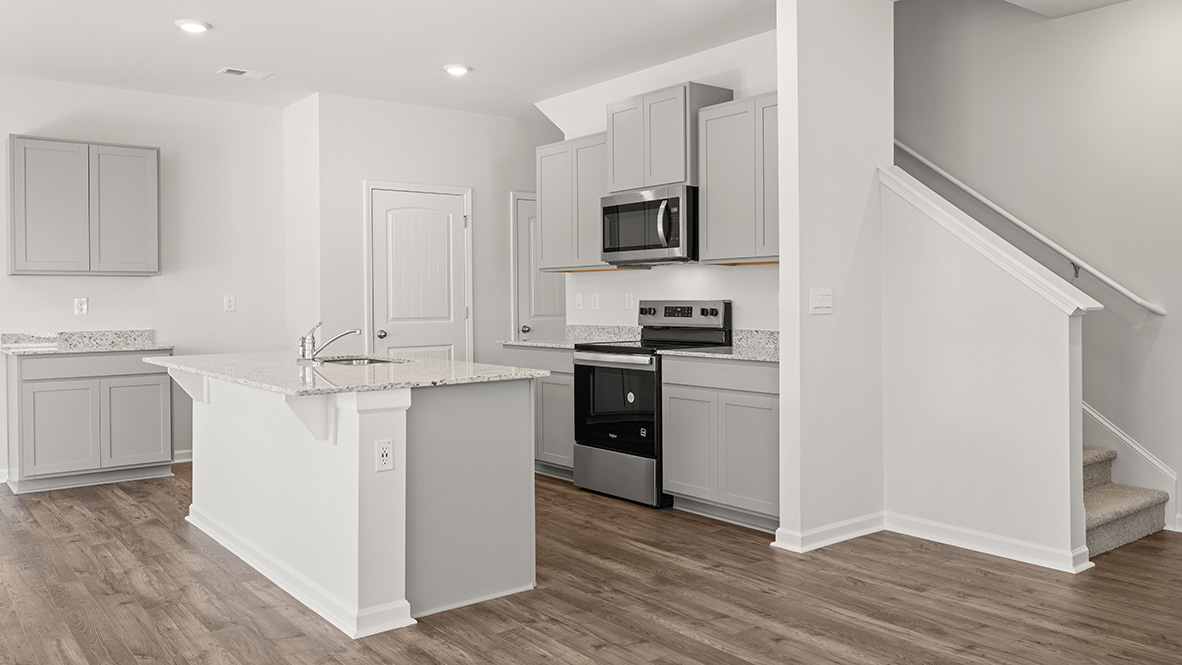 Modern kitchen with gray cabinets, granite countertops, and stainless steel appliances, featuring a central island. Warm wood flooring enhances a clean, inviting space.