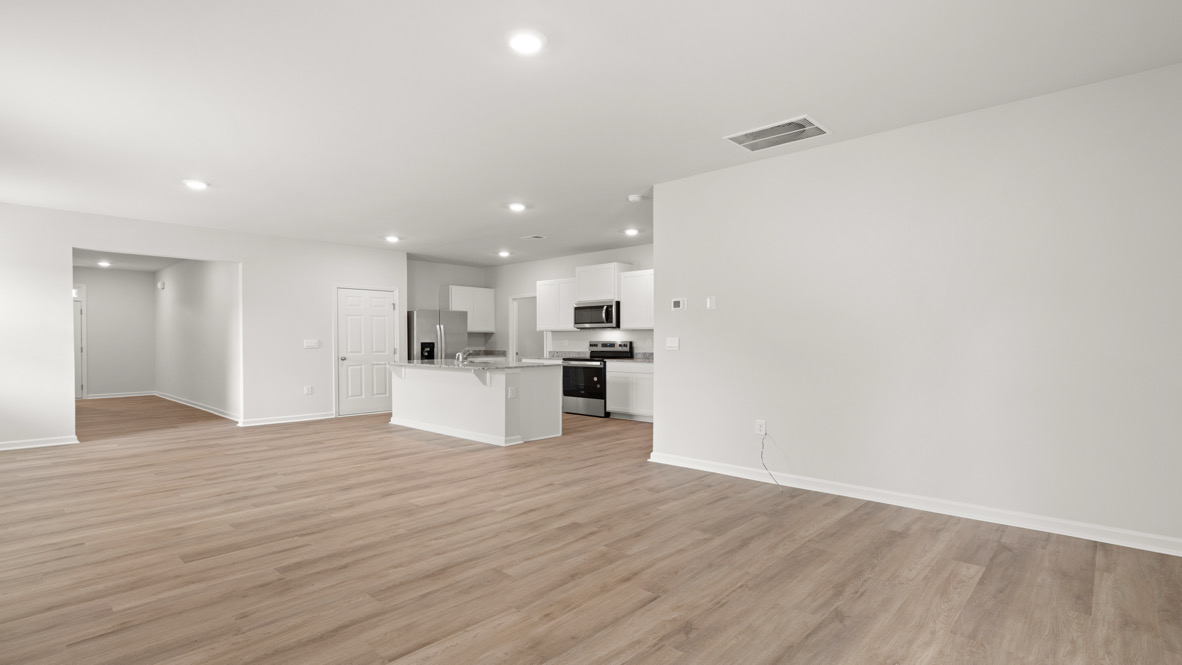 Spacious open-plan kitchen with sleek white cabinets, stainless steel appliances, and light wood flooring, creating a modern, minimalist ambiance.