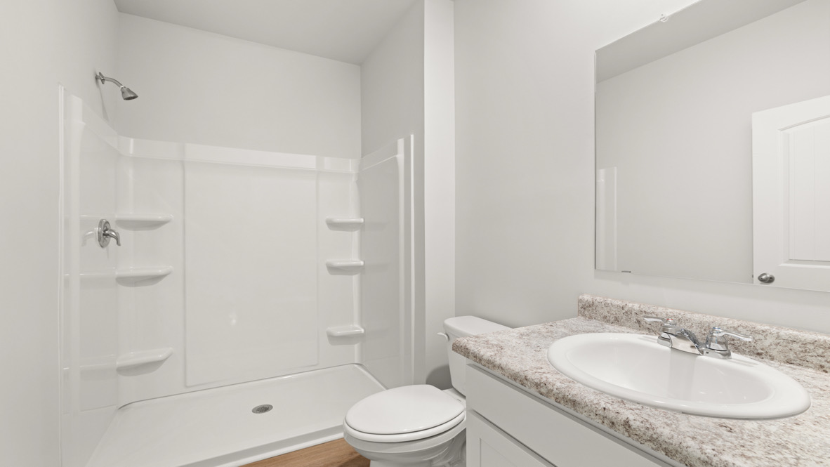 Bright bathroom with a white shower stall, shelves, and chrome fixtures. Vanity with granite countertop, sink, faucet, mirror, and toilet. Clean and minimal.
