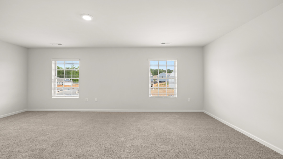 Empty room with beige carpet and two windows on a light gray wall, offering a view of houses outside. Bright, minimalist, and spacious atmosphere.