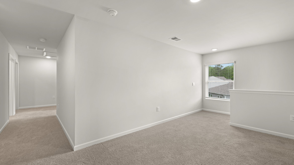 Hallway with beige carpet and white walls, leading to a room with a large window. Natural light illuminates the space, creating a calm atmosphere.