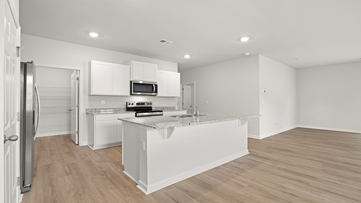 Modern kitchen with sleek white cabinets, stainless steel appliances, and a large granite island. The room features wood flooring and ample lighting.