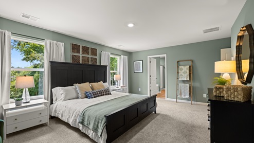 Spacious primary bedroom with beige carpet, green walls and two windows