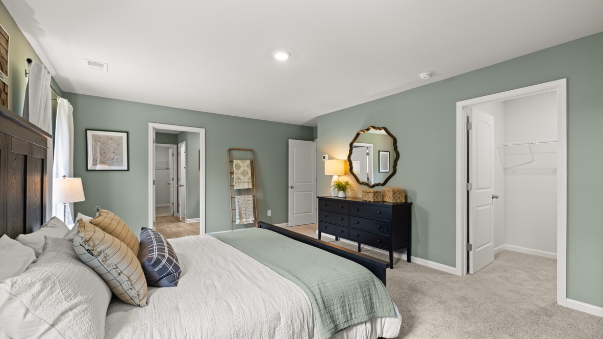 Spacious primary bedroom with beige carpet, green walls and two windows