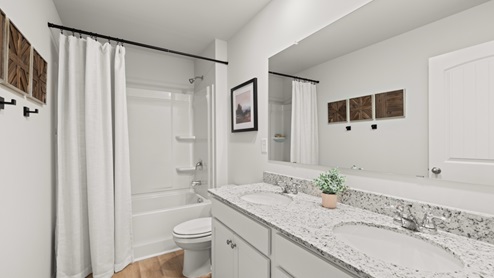 bathroom with dual vanity sinks, toilet and a shower