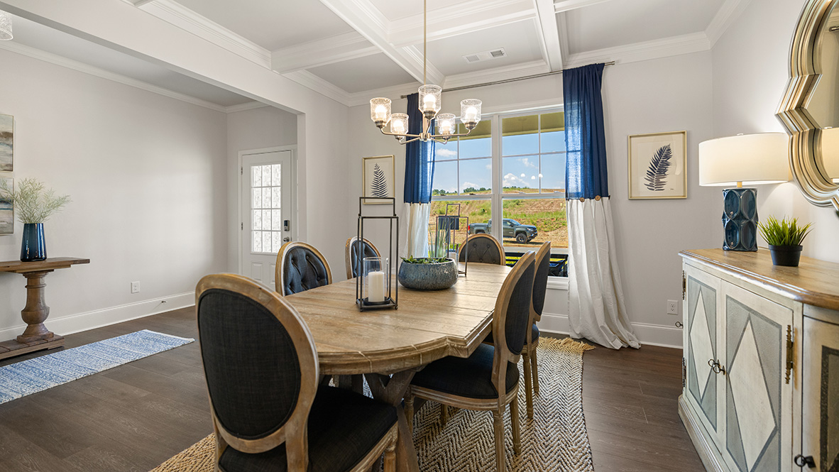 Bright dining room with white wainscoting, wooden floor, and a six-light chandelier. Large window on the left offers natural light and outdoor view.