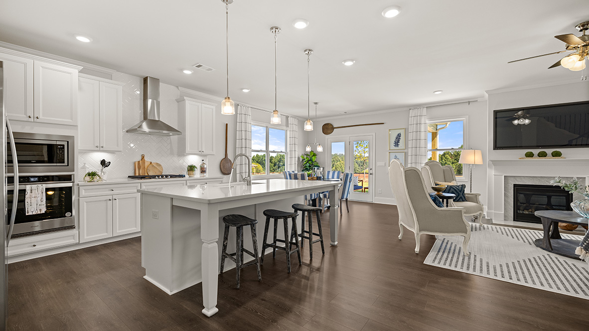 A modern kitchen with white cabinets, stainless steel appliances, and a large island. Wooden flooring and pendant lights add warmth to the bright space.