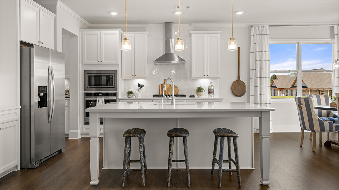 Bright modern kitchen with white cabinetry, chevron-patterned backsplash, and double stainless steel ovens. Hardwood flooring adds warmth.