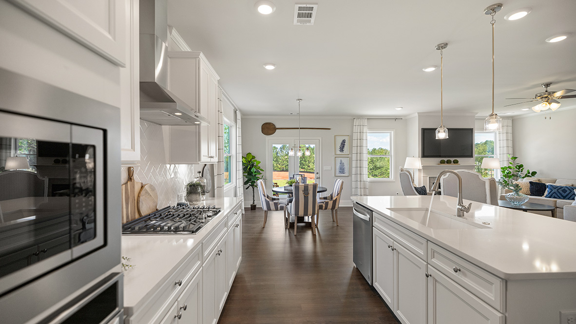 Spacious modern kitchen with white cabinets, an island, stainless steel appliances, and wood flooring. Bright lighting and an inviting, open floor plan.
