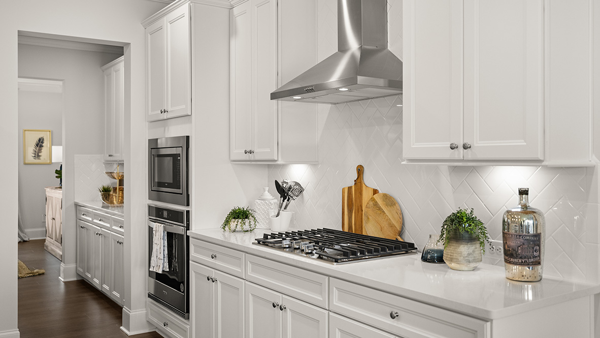 Spacious kitchen with white cabinetry, modern appliances, and a large island with a steel sink. Wood flooring adds warmth to the sleek, bright design.