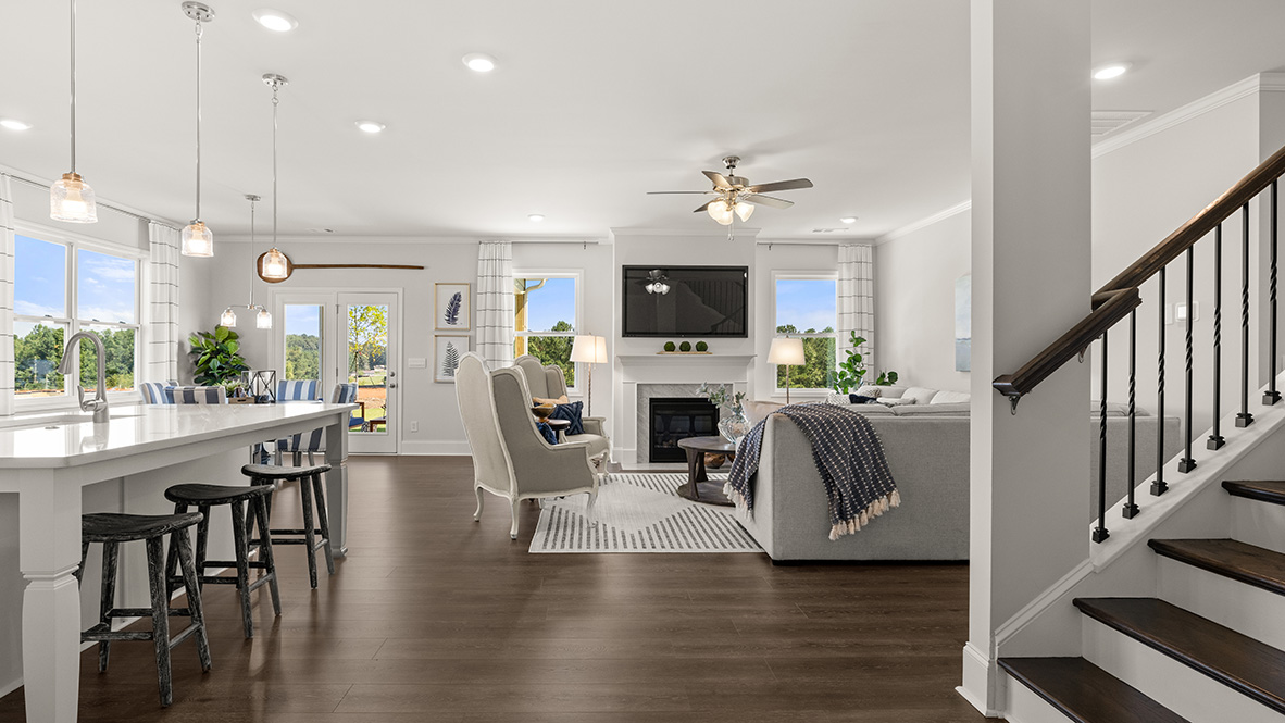 Spacious, living room with light gray walls, wood flooring, and a ceiling fan. A fireplace is centered between two bright windows.