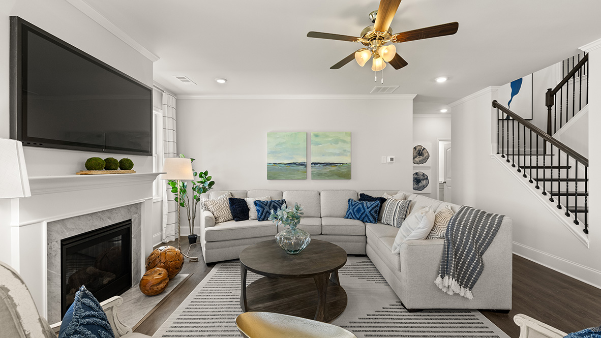 Spacious living room with hardwood floors, white walls, and large windows. Features a fireplace, ceiling fan, and modern kitchen area.