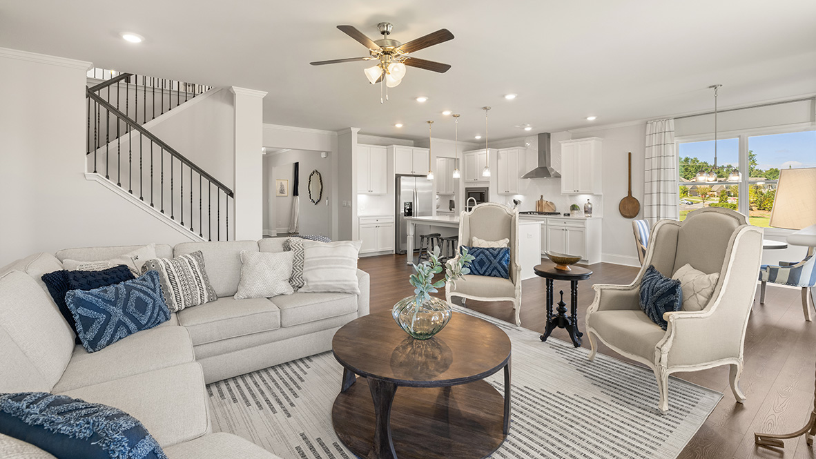 Spacious modern kitchen and living area with hardwood floors, white cabinets, and large island. A staircase with railing is visible on the left.