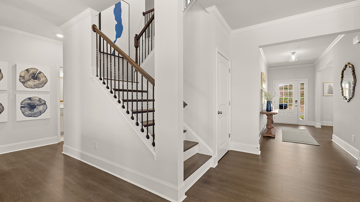 Spacious interior with wooden stairs featuring black railings, leading upwards. Warm-toned wooden floor and white walls create a clean, modern look.