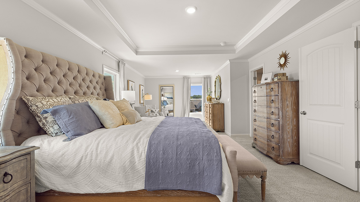Spacious, primary bedroom with beige carpet, white walls, and a tray ceiling. Open doors lead to a walk-in closet and a bright en-suite bathroom.