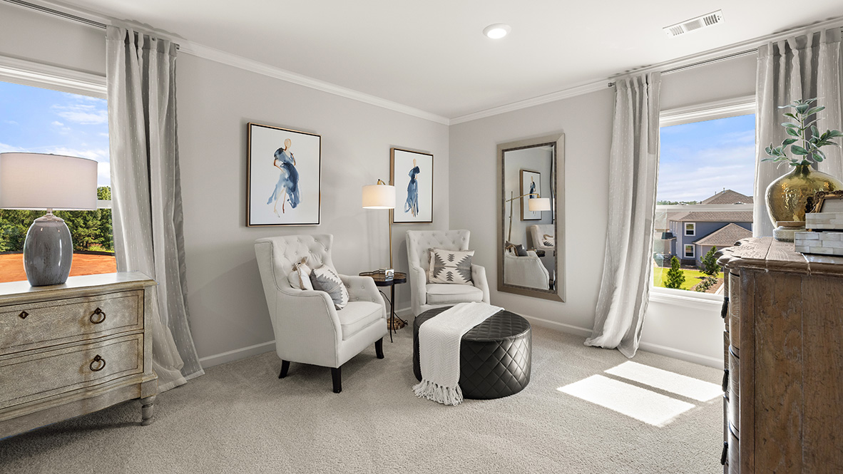 Bright room with beige carpet, three large windows with outdoor view, and an open door leading to a bathroom. The atmosphere is airy and fresh.