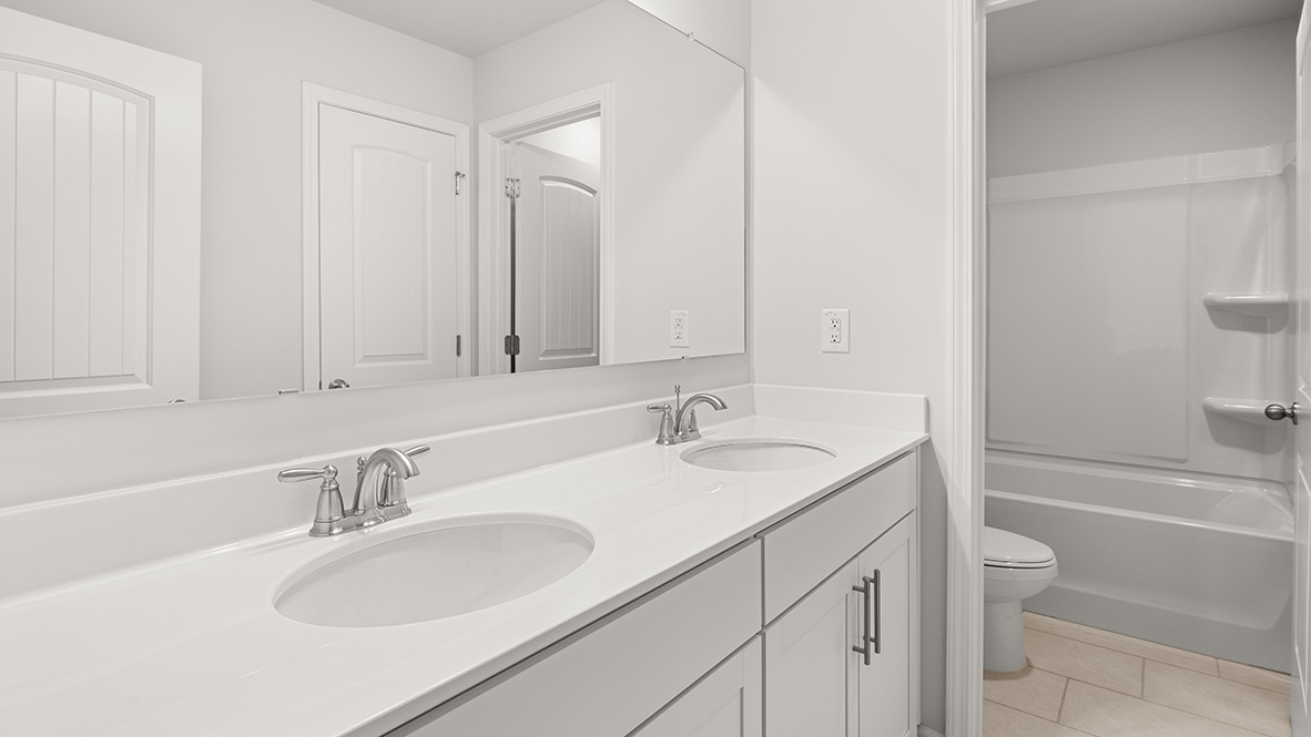 Sleek modern bathroom with a double sink vanity featuring chrome faucets, a large mirror, white cabinetry, and a shower-tub combo in a bright setting.