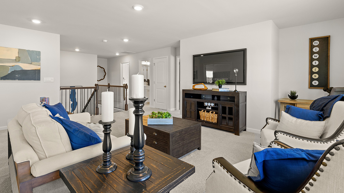 Upstairs hallway with beige carpet, wood and metal railing, and recessed lighting. Doors lead to a bathroom with white cabinets and adjacent rooms.