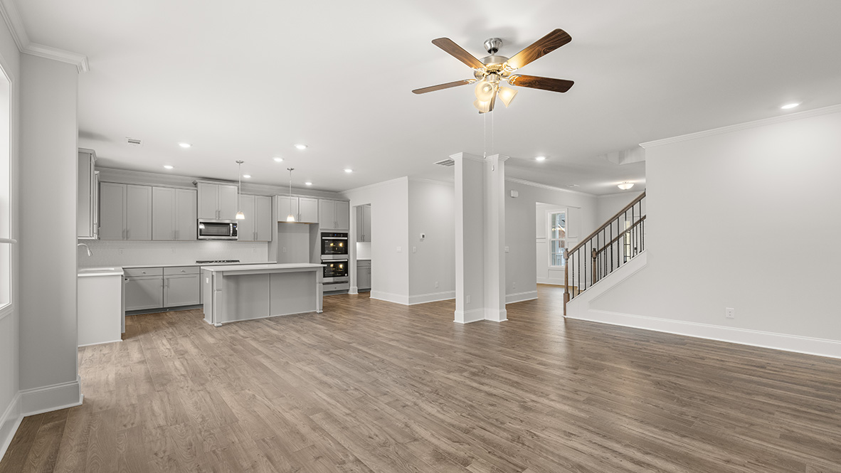 Spacious open-concept living area with hardwood floors, modern kitchen with gray cabinets, island, stainless appliances, and ceiling fan. Bright and inviting.
