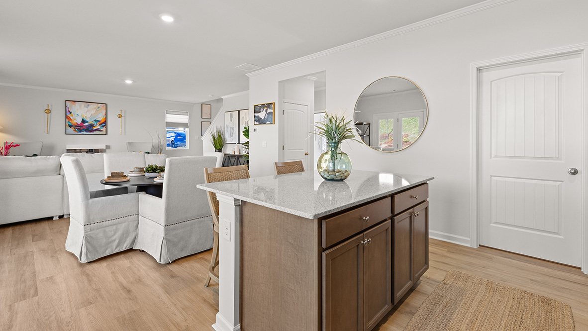 Large kitchen island with white countertops, white tile backsplash and brown shaker cabinets.