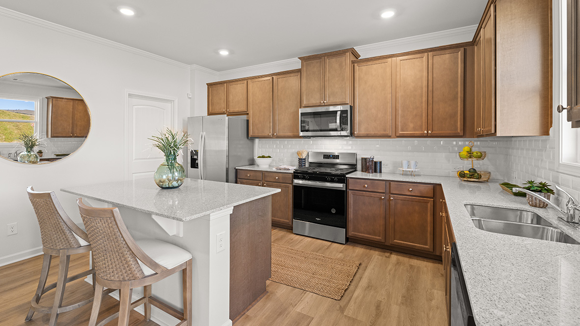Large kitchen island with white countertops, white tile backsplash and brown shaker cabinets.