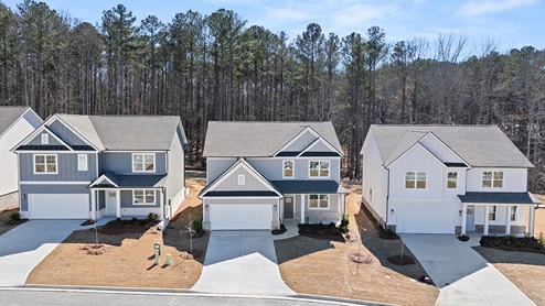 Multiple two-story elevations with white, gray and blue siding, white trim, brick details and trees in background.