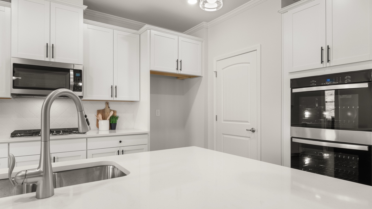Full kitchen and kitchen island with white and black countertop and brown shaker cabinets.