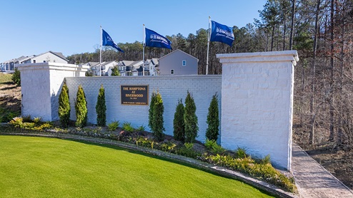 White brick Hamptons at Riverwood community monument with shrubbery and green grass.