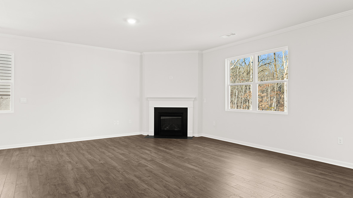 Spacious living room with brown flooring, white walls, a black fireplace and windows