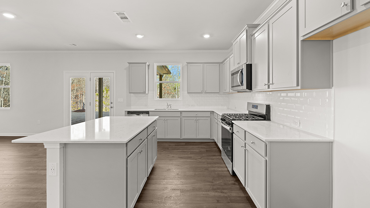 Kitchen has a large island, white countertops, grey shaker-style cabinets, white subway tile, stainless steel appliances, and a window in front of the kitchen sink.