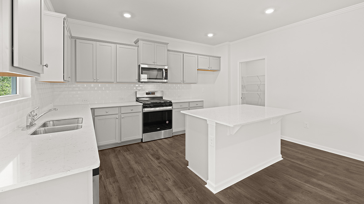 Dining room view of the kitchen with white countertops, grey shaker-style cabinets, white subway tile, stainless steel appliances, and the pantry.