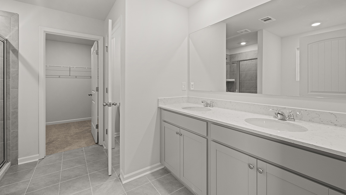 Ensuite bathroom with a double vanity sink, white countertops, grey shaker-style cabinets, and a walk-in closet.