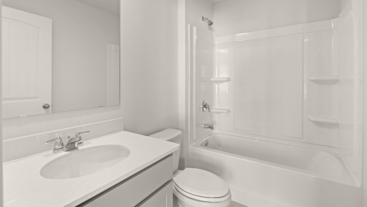 A bathroom with a tub shower, toilet, sink with white countertop, and gray cabinets.
