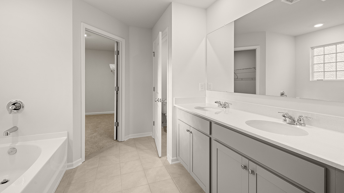 Interior primary bathroom with double sink, bathtub and walk-in closet