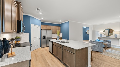 Kitchen featuring an island with a sink, natural wood color beveled flat panel cabinets, white subway tiles backsplash and stainless steel appliances.