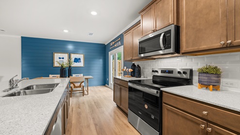 Kitchen featuring an island with a sink, granite countertops, natural wood colored beveled flat panel cabinets and a dining room with a glass back door.
