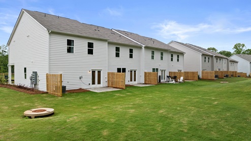 View from the home's backyard with two windows, a glass back door, and a small patio.