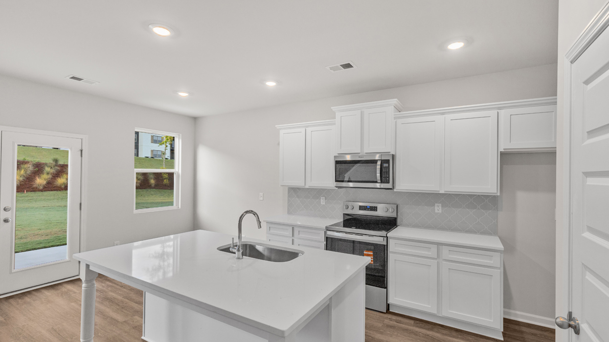 overview of kitchen island with sink and spacious white cabinets and access to back patio