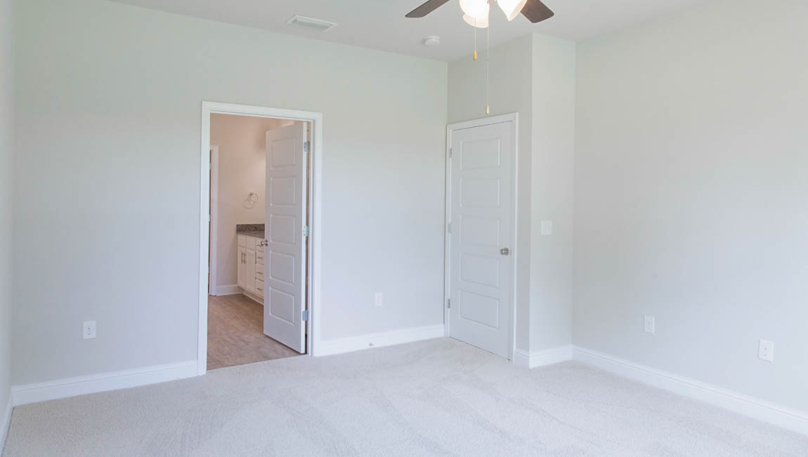 Relax in this modern D.R. Horton primary bedroom with plush carpet and ceiling fan.