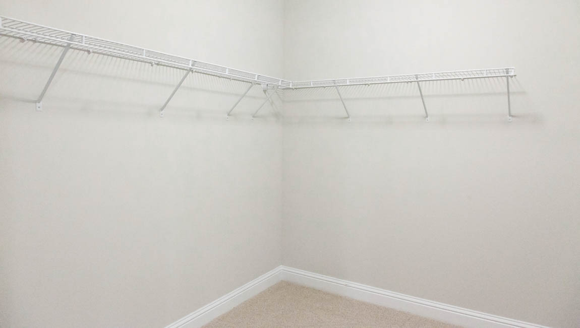 Spacious primary walk in closet with shelving a neutral color palette.