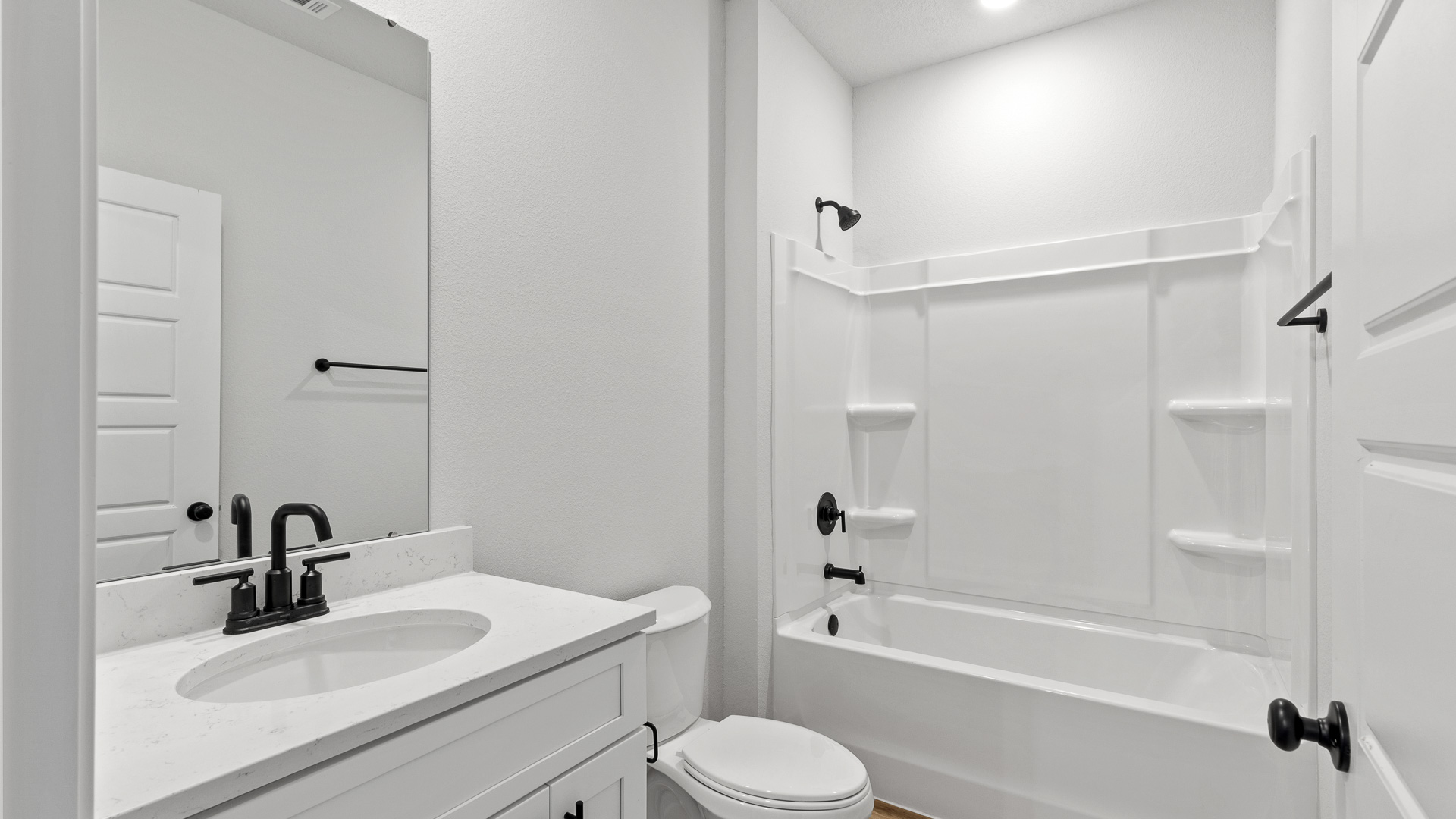 Bright guest bathroom with shower tub combination, mirror, and bath accessories in a new D.R. Horton home.