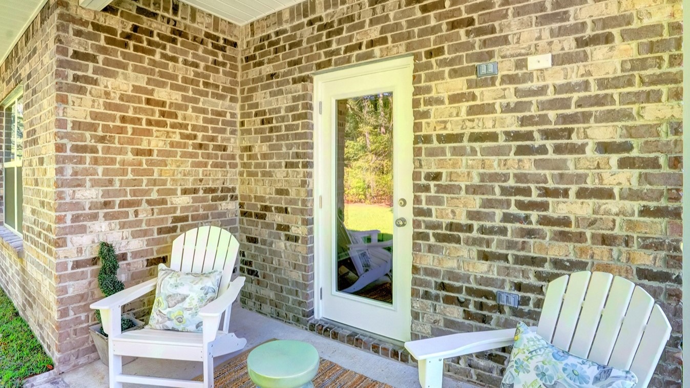 Exterior door inset in brick wall flanked with white chairs.