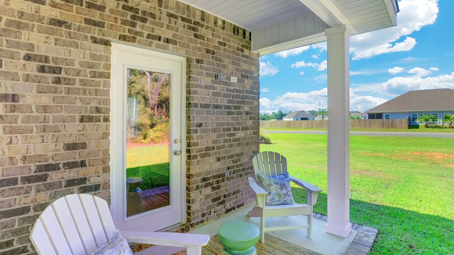 Back porch with brick exterior, columns and white chairs.
