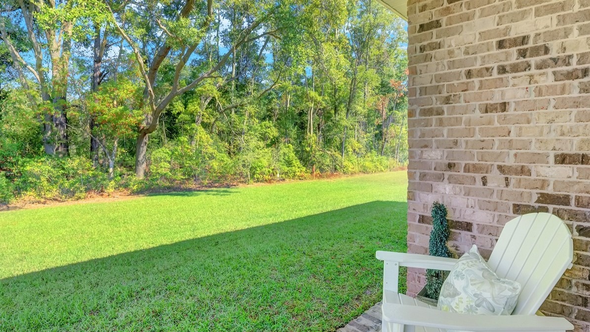 Side yard with green grass, brick side of home and white chair.