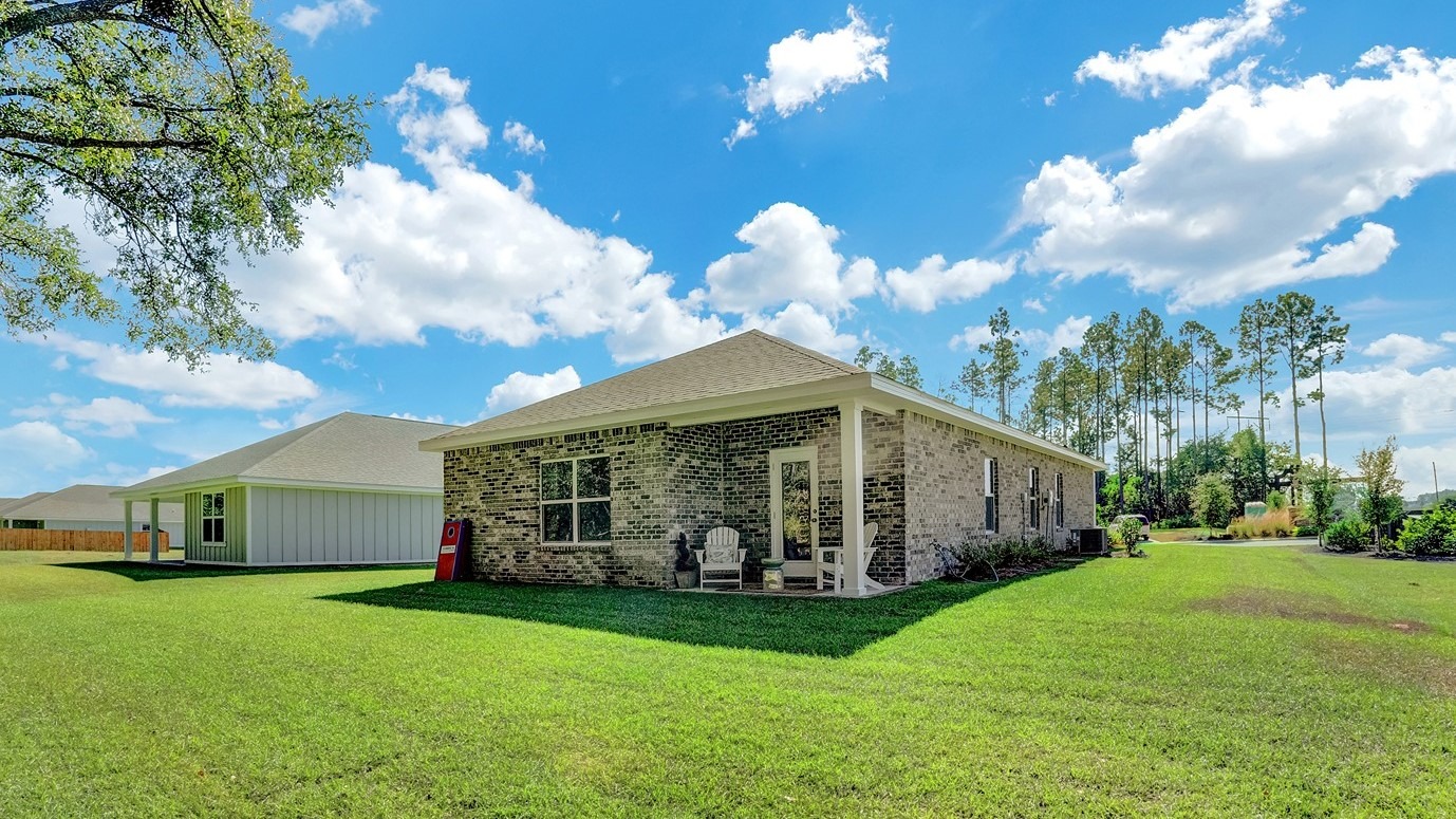 Bright green grass backyard surrounding brick home with porch.