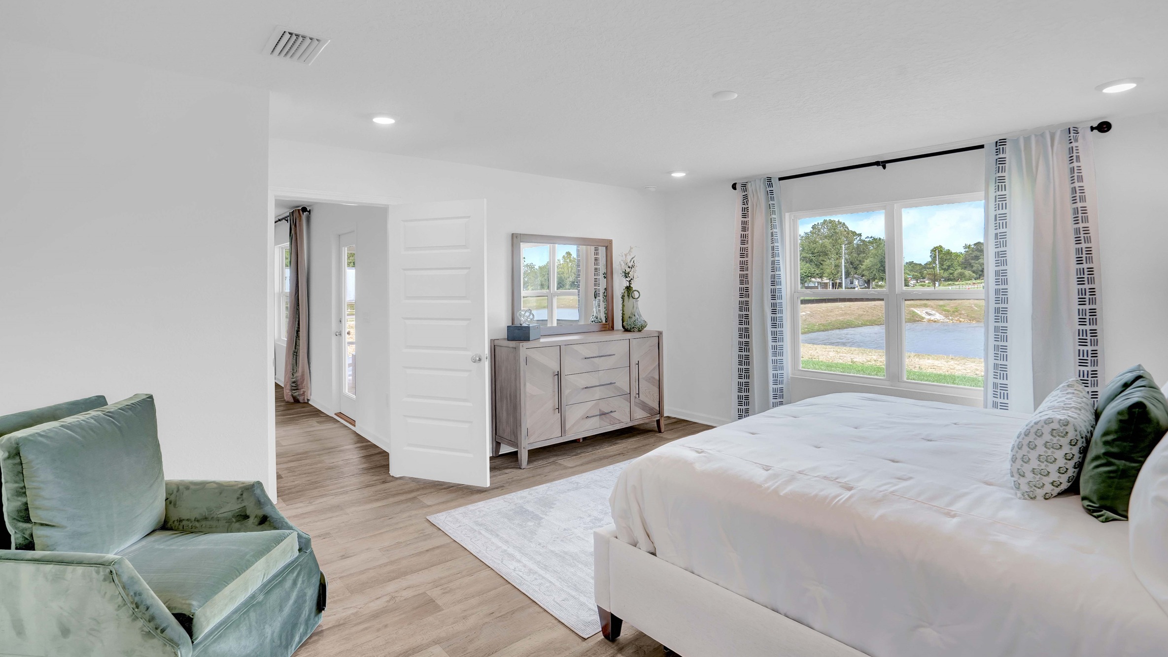 Ryder floor plan spacious primary bedroom with large bed, dresser, and accent chair.