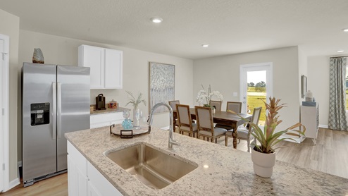Kitchen peninsula with white cabinets, granite countertops, and stainless-steel appliances overlooking dining area.